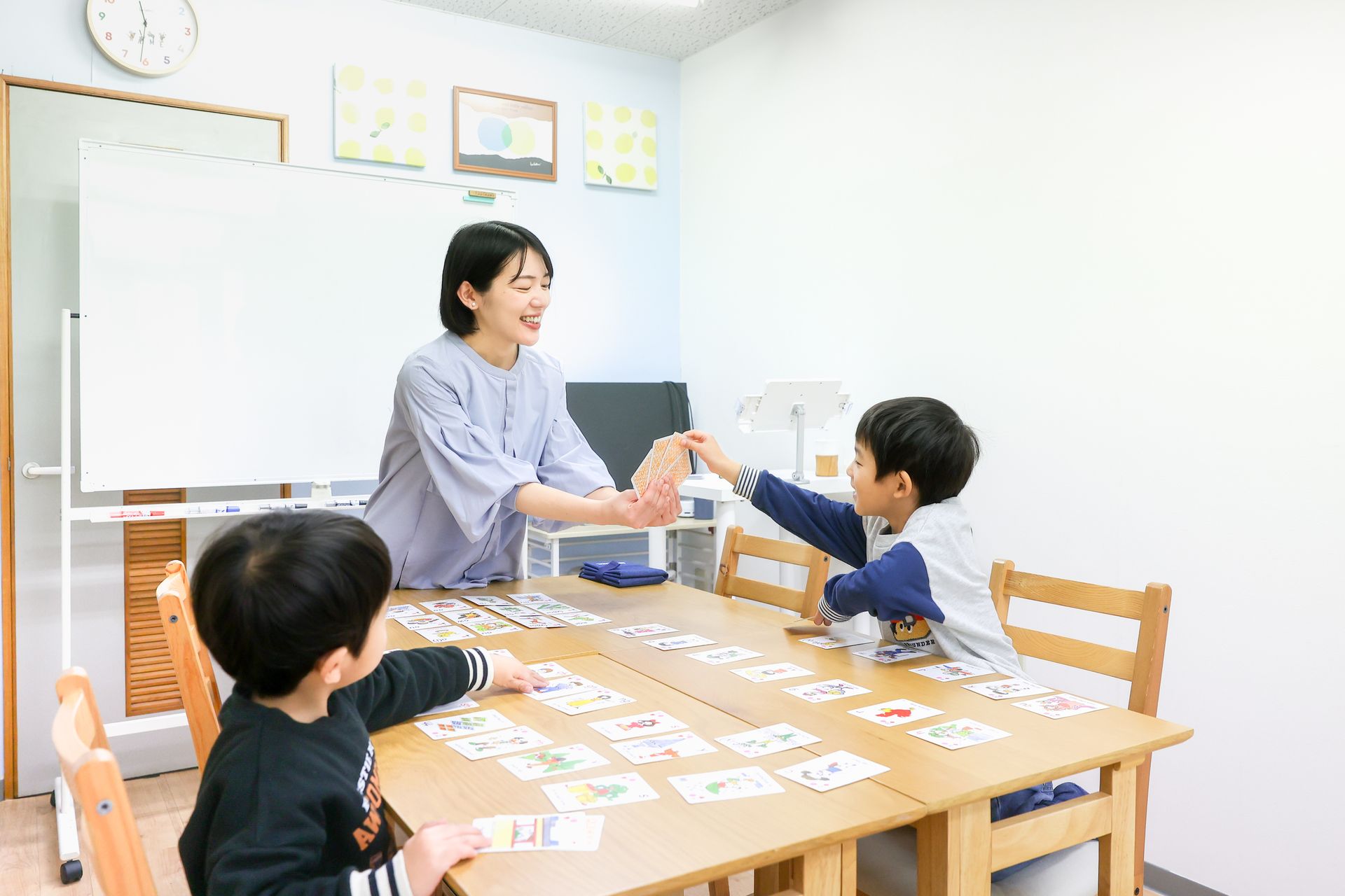 テーブルに並べたカードを使って、講師と子どもたちが英語を学ぶようす