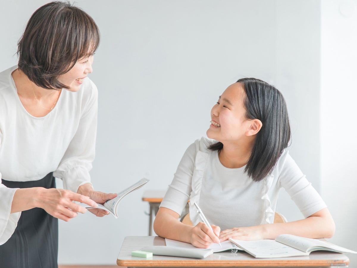 机で学ぶ生徒に、そばで声をかける先生